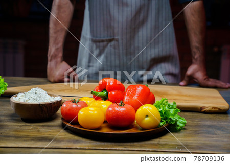 a wooden bowl of flour and vegetables on the kitchen table. man in an apron. 78709136