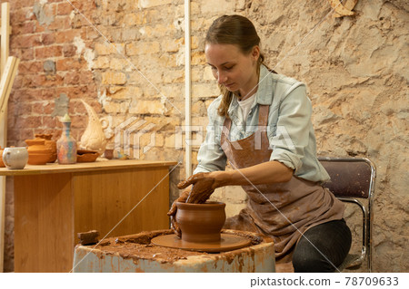 Female potter sculpts a clay pot. The sculptor works with clay on a potter's wheel and at a table Female potter sculpts a clay pot. The sculptor works with clay on a potter's wheel and at a table 78709633