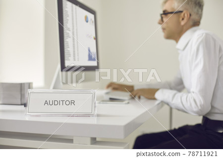 Nameplate that reads AUDITOR with a senior man working on a computer in the background 78711921