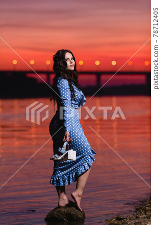 Beautiful young girl with long dark wavy hair standing at the bank of the river Beautiful young girl with long dark wavy hair standing at the bank of the river 78712405