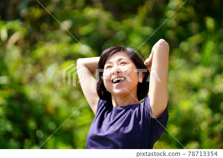 A smiling middle-aged woman taking a deep breath in the green, upper body portrait 78713354