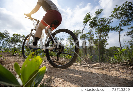 Woman cyclist cycling on mountain top forest trail 78715269