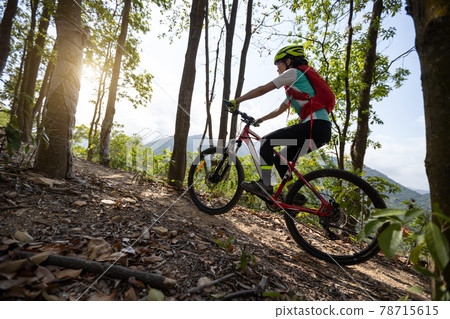Woman cyclist cycling on mountain top forest trail Woman cyclist cycling on mountain top forest trail 78715615