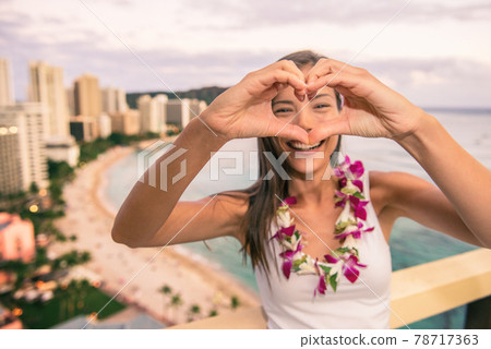 Happy Hawaii Waikiki beach tourist doing heart shape with hands enjoying Honolulu city travel vacation in luxury resort balcony view of sunset. 78717363