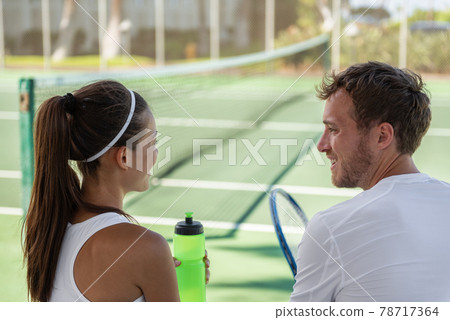 Tennis players mixed doubles talking after match on hard court outside at tennis club. Private teacher man giving lesson to Asian woman or couple having fun. 78717364