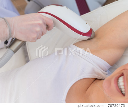 Doctor doing laser hair removal on a woman's armpit in the salon. An alternative way to permanently remove unwanted body hair Doctor doing laser hair removal on a woman's armpit in the salon. An alternative way to permanently remove unwanted body hair 78720473