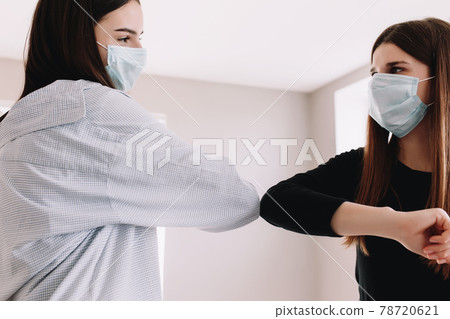 Two smiling girls in protective face mask say hello with elbow 78720621