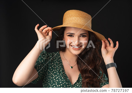 Beautiful young woman with straw hat posing against black background Beautiful young woman with straw hat posing against black background 78727197