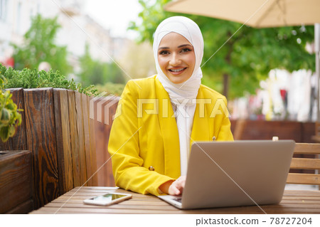 Beautiful smiling muslim woman with laptop at cafe Beautiful smiling muslim woman with laptop at cafe 78727204