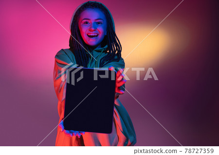 Holding tablet, crazy excited. Caucasian young woman's portrait on black studio background in neon light. Beautiful male model in white shirt. Holding tablet, crazy excited. Caucasian young woman's portrait on black studio background in neon light. Beautiful male model in white shirt. 78727359