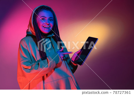 Holding tablet, crazy excited. Caucasian young woman's portrait on black studio background in neon light. Beautiful male model in white shirt. Holding tablet, crazy excited. Caucasian young woman's portrait on black studio background in neon light. Beautiful male model in white shirt. 78727361