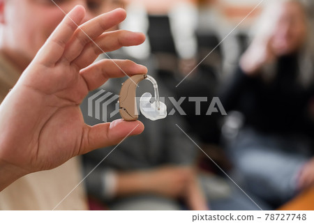 A young man puts on a hearing aid. Portable sound amplifier for the deaf and hearing impaired A young man puts on a hearing aid. Portable sound amplifier for the deaf and hearing impaired 78727748