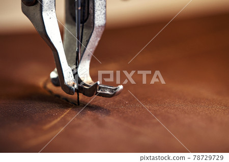 Machine head with a needle close-up, a sewing machine makes a seam on a piece of leather. Machine head with a needle close-up, a sewing machine makes a seam on a piece of leather. 78729729