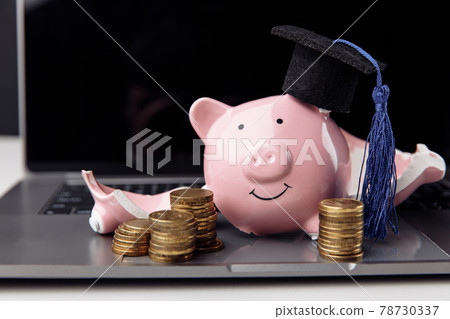 Broken piggy bank in graduation cap on laptop. Expensive education and scholarship concept 78730337