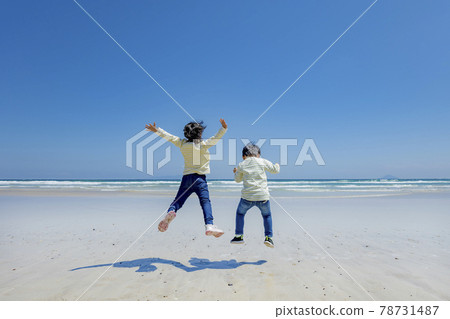 Back view of older sister and younger brother jumping at the beach 78731487