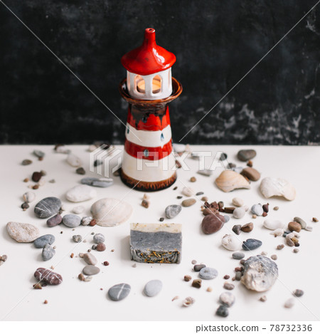 A small decorative lighthouse with sea shells and pebbles. Summer, holidays and vacation concept A small decorative lighthouse with sea shells and pebbles. Summer, holidays and vacation concept 78732336