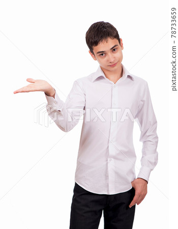 Smiling guy in white clothes on a white background looks at the camera and shows an empty palm. Cheerful young man in white shirt shows on blank space 78733659