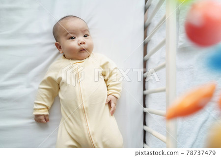 Happy Smiling Asian Newborn baby boy lying on bed or cot having fun playing with mobile. Happy Smiling Asian Newborn baby boy lying on bed or cot having fun playing with mobile. 78737479