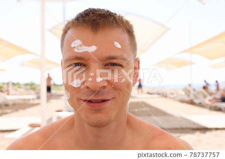 Man sitting on beach with sunscreen on his face Man sitting on beach with sunscreen on his face 78737757