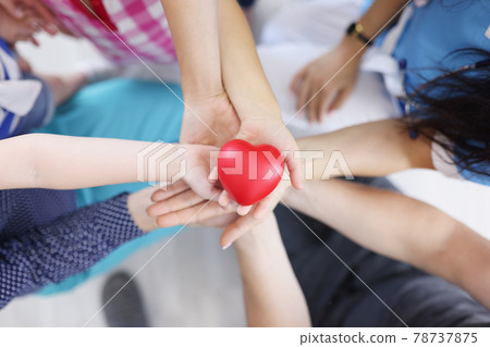 Many adults and children hands are holding plastic toy heart top view Many adults and children hands are holding plastic toy heart top view 78737875