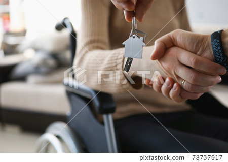 Disabled woman in wheelchair shaking hands with man with keys to new apartment closeup Disabled woman in wheelchair shaking hands with man with keys to new apartment closeup 78737917