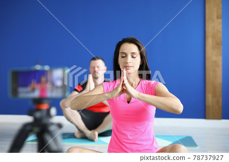 Man and woman sitting in lotus position on gymnastic mats in front of camera 78737927