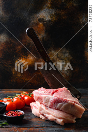 Farm fresh Pork Belly,Raw pork cutlet with oil and spices for grill or cooking on wooden dark planks over rustic background, and chopping cleaver butcher knife, side view spacr for text vertical. 78738222