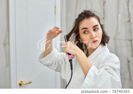 woman using a hair straightener in bathroom. 78740365