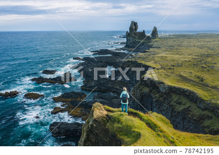 Man hiker in yellow jacket stand on the peak of the rock in outdoor park in Iceland. Londrangar Man hiker in yellow jacket stand on the peak of the rock in outdoor park in Iceland. Londrangar 78742195