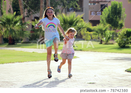 Happy sisters run on footpath in tropical resort Happy sisters run on footpath in tropical resort 78742380