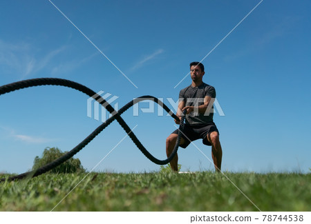 Male athlete on the outdoor in the park, exercises for endurance, using a thick rope, for cross fitness. European Male athlete on the outdoor in the park, exercises for endurance, using a thick rope, for cross fitness. European 78744538