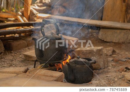 Old teapot for boiling water by using traditional kettle and fire, water heater at wooden kitchen at local home. People lifestyle. Old teapot for boiling water by using traditional kettle and fire, water heater at wooden kitchen at local home. People lifestyle. 78745889