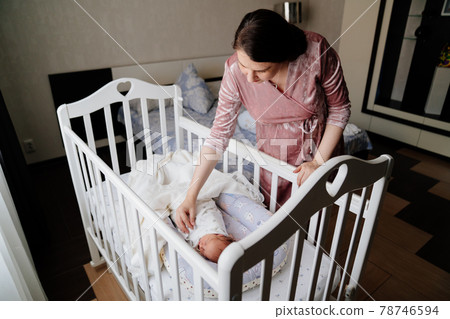 Mom straighten the blanket at the sleeping in the crib of the newborn. Mom straighten the blanket at the sleeping in the crib of the newborn. 78746594