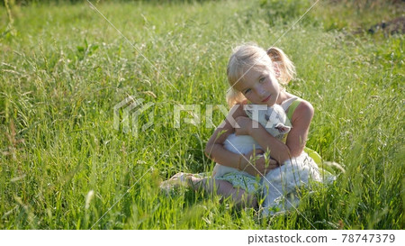 A six-year-old girl in a meadow gently hugs a small white goat. A six-year-old girl in a meadow gently hugs a small white goat. 78747379