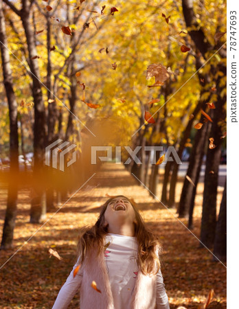 Beautiful little girl throwing fallen leaves, playing in the park; autumn/nature background Beautiful little girl throwing fallen leaves, playing in the park; autumn/nature background 78747693