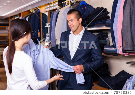 Female shopping assistant offering various shirts in mens cloths store 78758385
