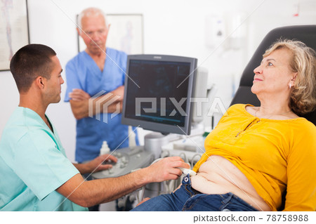 Man examines a mature woman at abdomen with ultrasound Man examines a mature woman at abdomen with ultrasound 78758988