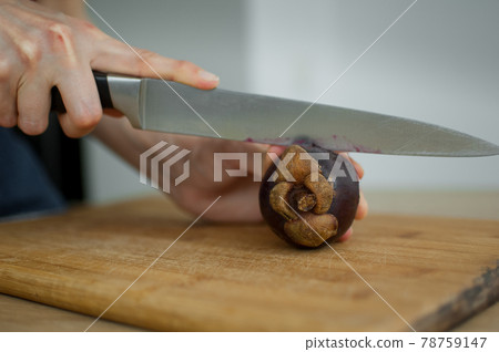 Female hands is cutting with knife a fresh ripe mangosteen on a cut wooden board. Exotic fruits, healthy eating concept Female hands is cutting with knife a fresh ripe mangosteen on a cut wooden board. Exotic fruits, healthy eating concept 78759147
