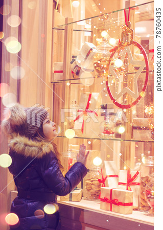 Beautiful little girl in front of confectionery shop, decorated with wrapped gift boxes and candies. Christmas concept, window shopping 78760435
