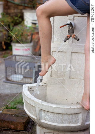 Little girl washing her feet on the decorative garden faucet Little girl washing her feet on the decorative garden faucet 78762267