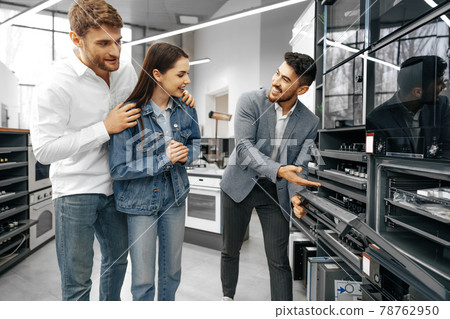 Male shop assistant helps young couple to choose new home appliance 78762950