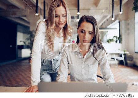 Two young female colleagues discussing business project together in office Two young female colleagues discussing business project together in office 78762992