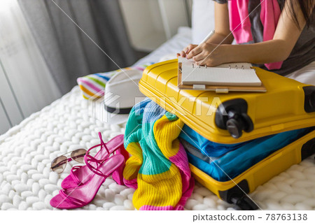 Female hands writing checklist of clothes shoes and accessories packing suitcase to travel vacation Female hands writing checklist of clothes shoes and accessories packing suitcase to travel vacation 78763138