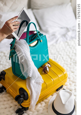 Woman hands ready travel journey putting tablet pc into handbag packing baggage at bedroom Woman hands ready travel journey putting tablet pc into handbag packing baggage at bedroom 78763195