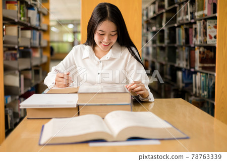 Young Asian women are searching for books and reading from the bookshelves in the college library to research and develop themselves in education Young Asian women are searching for books and reading from the bookshelves in the college library to research and develop themselves in education 78763339