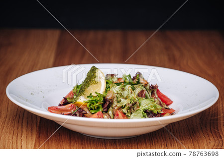 White Plate with Salad Stands on a Wooden Table in a Restaurant White Plate with Salad Stands on a Wooden Table in a Restaurant 78763698
