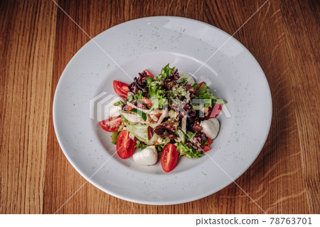 White Plate with Salad Stands on a Wooden Table in a Restaurant White Plate with Salad Stands on a Wooden Table in a Restaurant 78763701