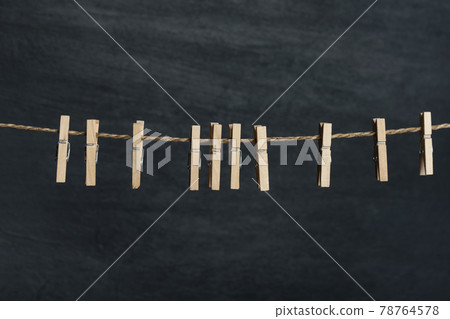Several wooden cloth clips in rope waiting for clothes to come after laundry. Black wall on the background Several wooden cloth clips in rope waiting for clothes to come after laundry. Black wall on the background 78764578