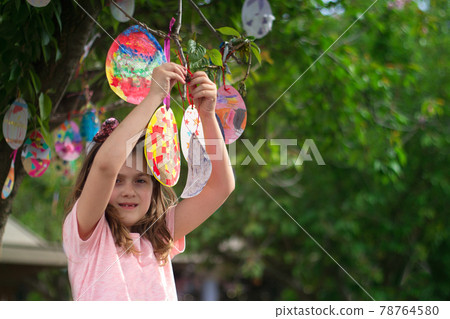 Cute little girl hanging on the tree her Easter cards in egg shape, for good luck and with good wishes Cute little girl hanging on the tree her Easter cards in egg shape, for good luck and with good wishes 78764580