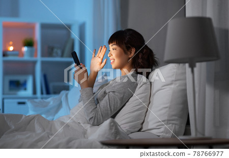 woman with phone having video call in bed at night woman with phone having video call in bed at night 78766977